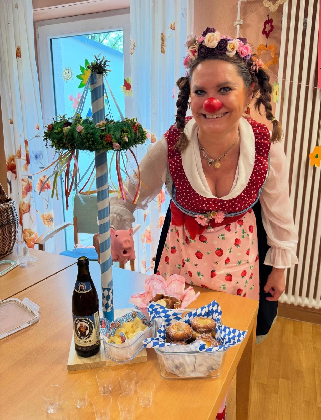 Mitarbeiterin mit roter Clownsnase neben einem geschmückten Maibaum
