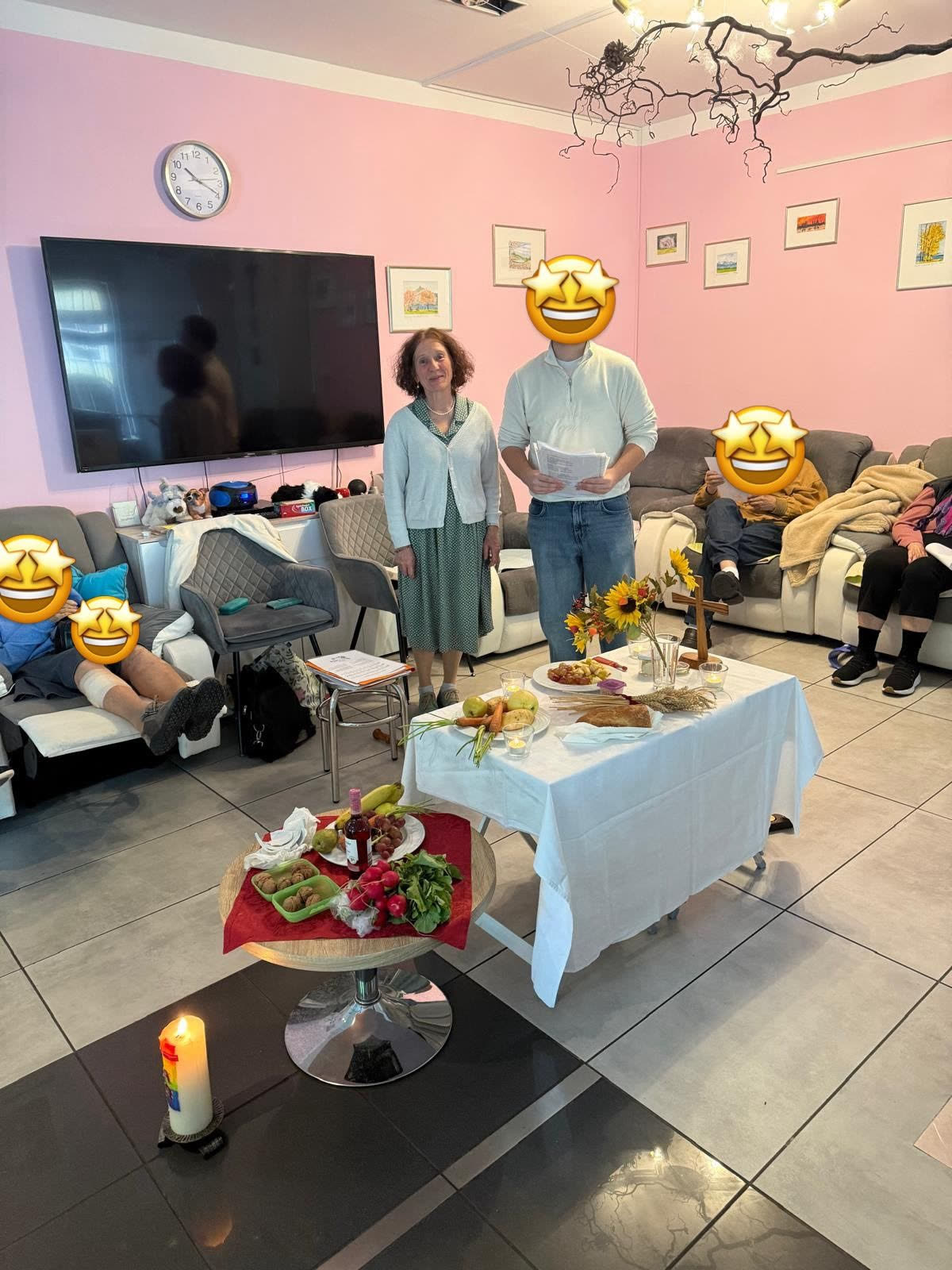 Gedeckter Tisch mit Kreuz, Erntegaben und Kerze, davor die Runde im Salon